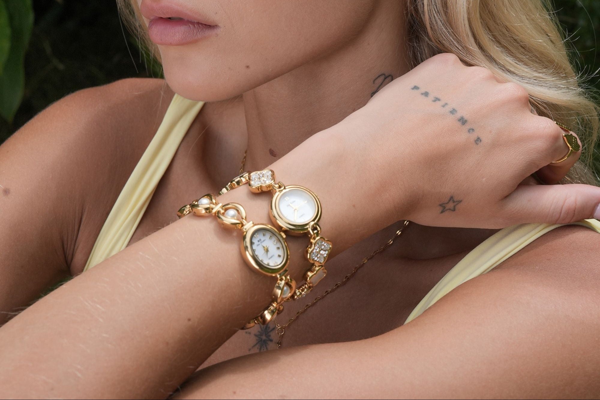 Woman wearing gold jewelry including earrings, bracelet, and ring with a natural background
