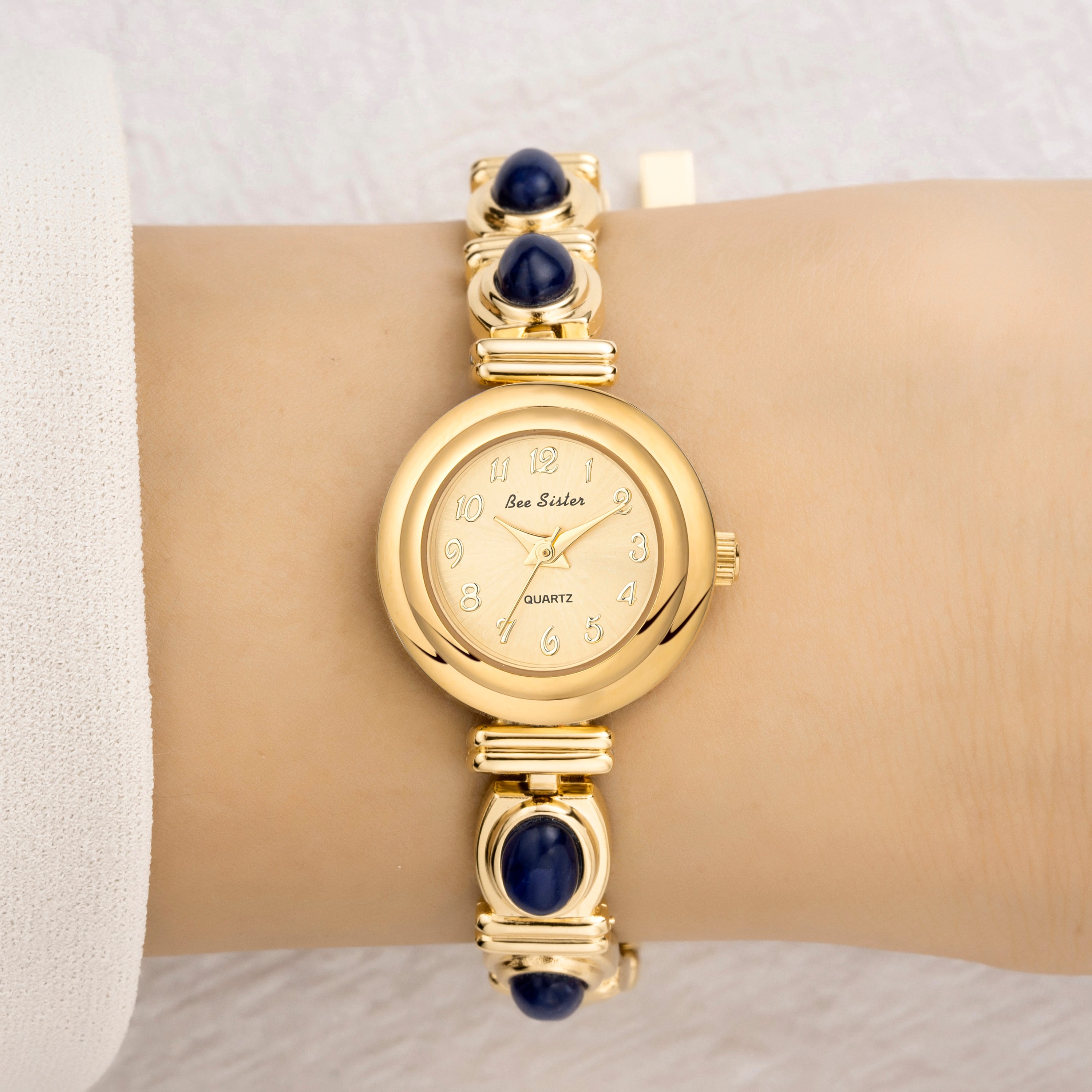 Gold wristwatch with blue gemstones on a wrist against a neutral background