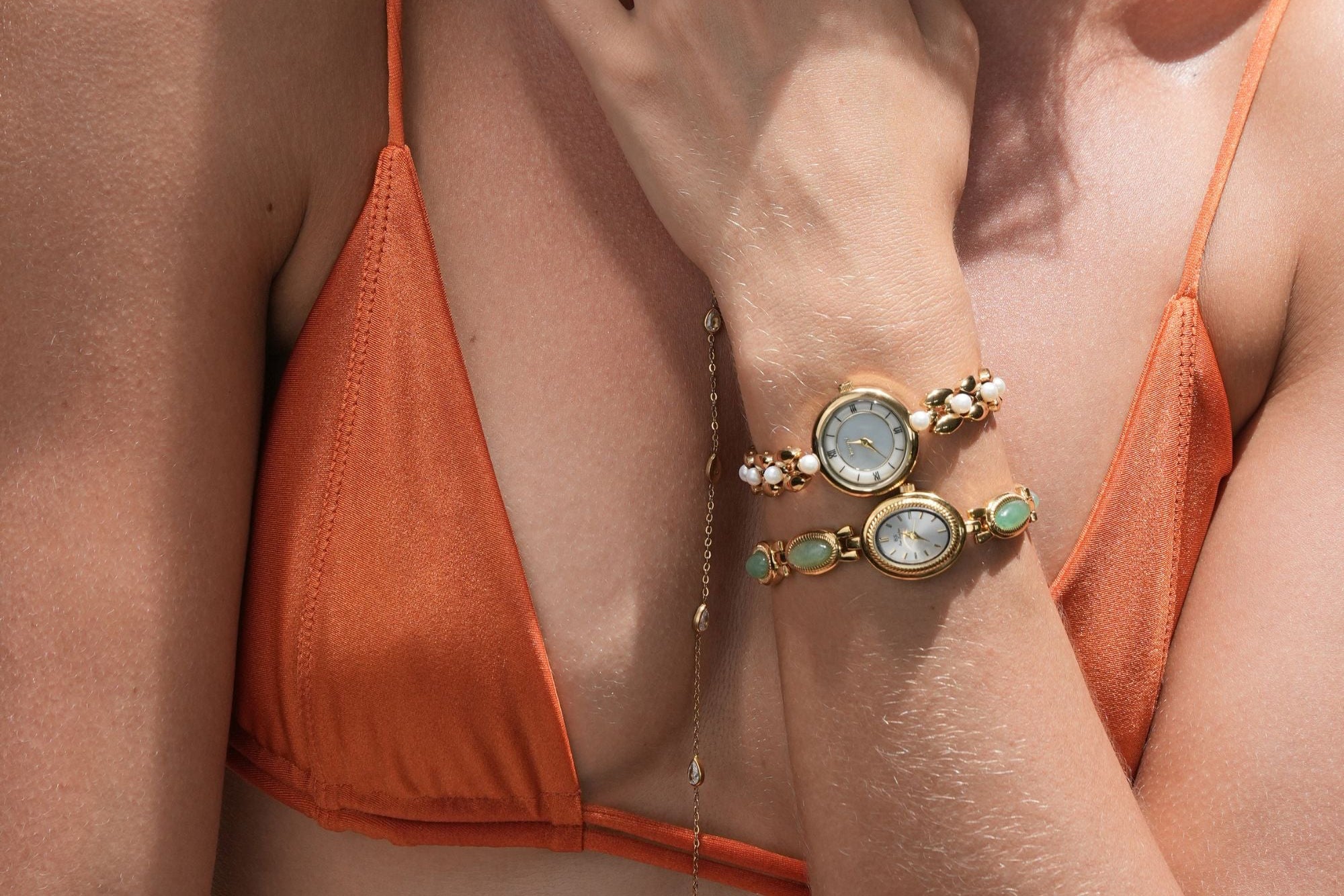 Woman wearing an orange bikini with a close-up of her hand and jewelry.