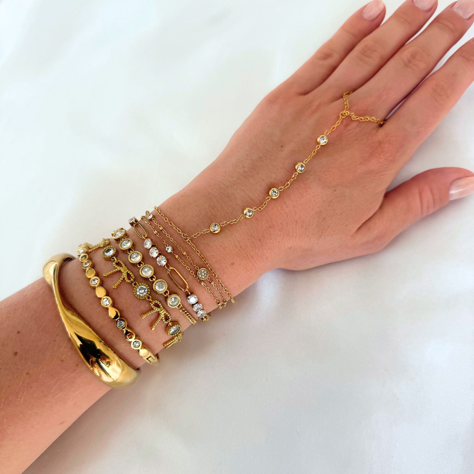 Hand wearing multiple gold bracelets on a white background